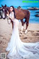 A woman in a wedding dress standing next to a horse on the beach.