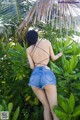 A woman in a black top and denim shorts standing in front of a palm tree.