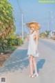 A woman in a white dress and a straw hat standing on a road.