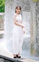 A woman in a white dress standing in front of a fountain.