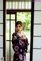 A woman in a black kimono standing in front of a door.