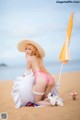 A woman in a bikini and hat sitting on the beach.